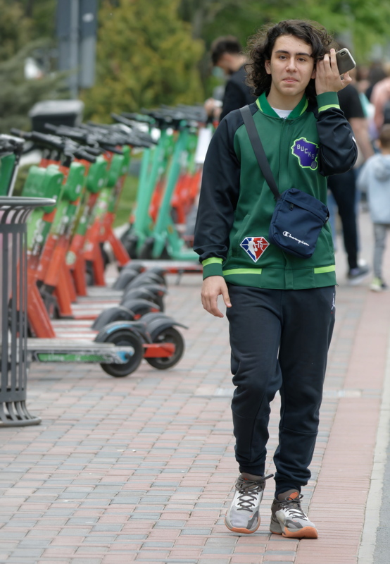28 - Person walking past a row of parked electric rental scooters on a paved sidewalk